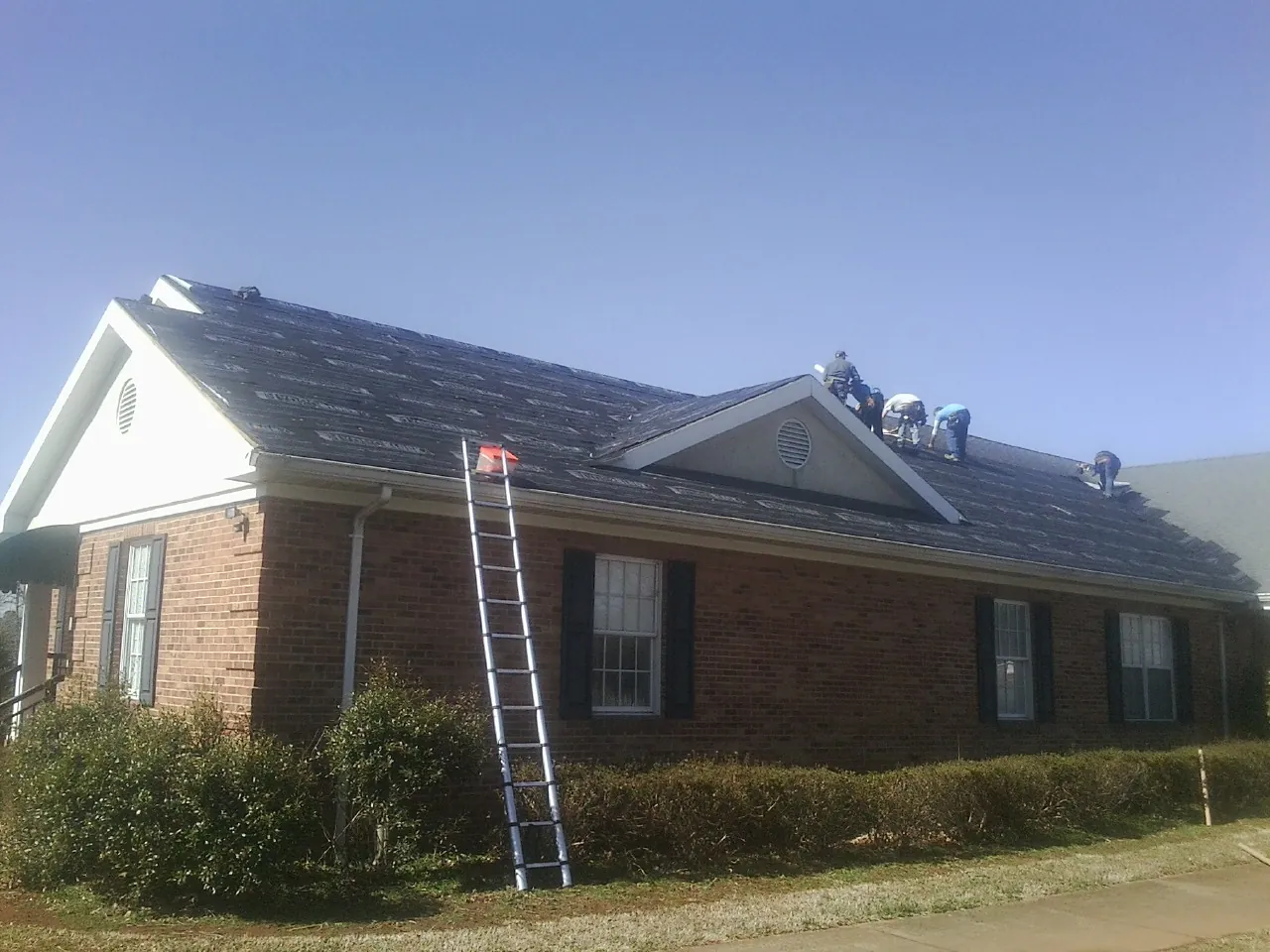 Crew tearing shingles off a brick ranch roof with a ladder set — Emergency Roof Repair work by our crew in Pelham